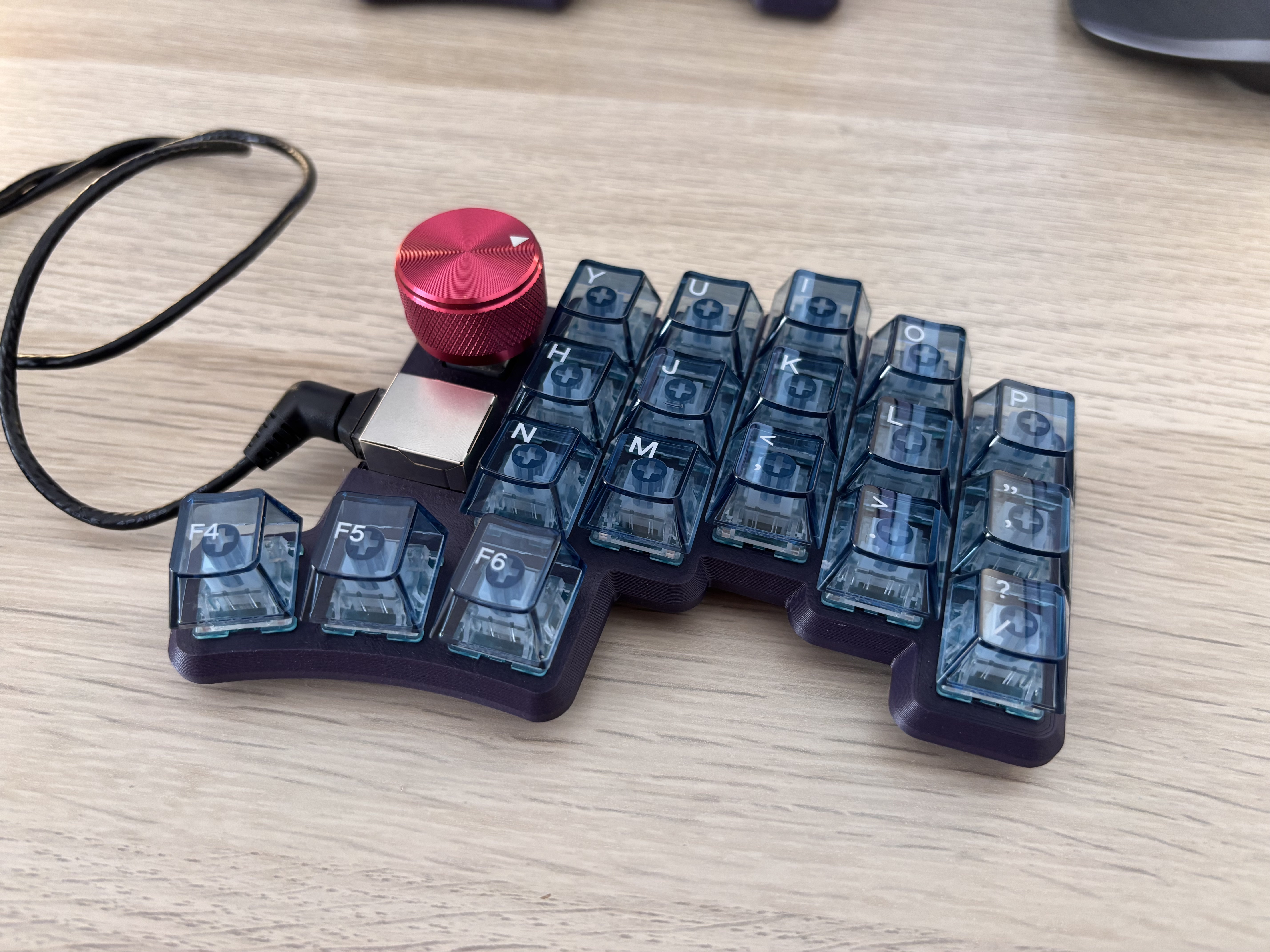 Half a split keyboard with transparent blue keycaps and a red dial