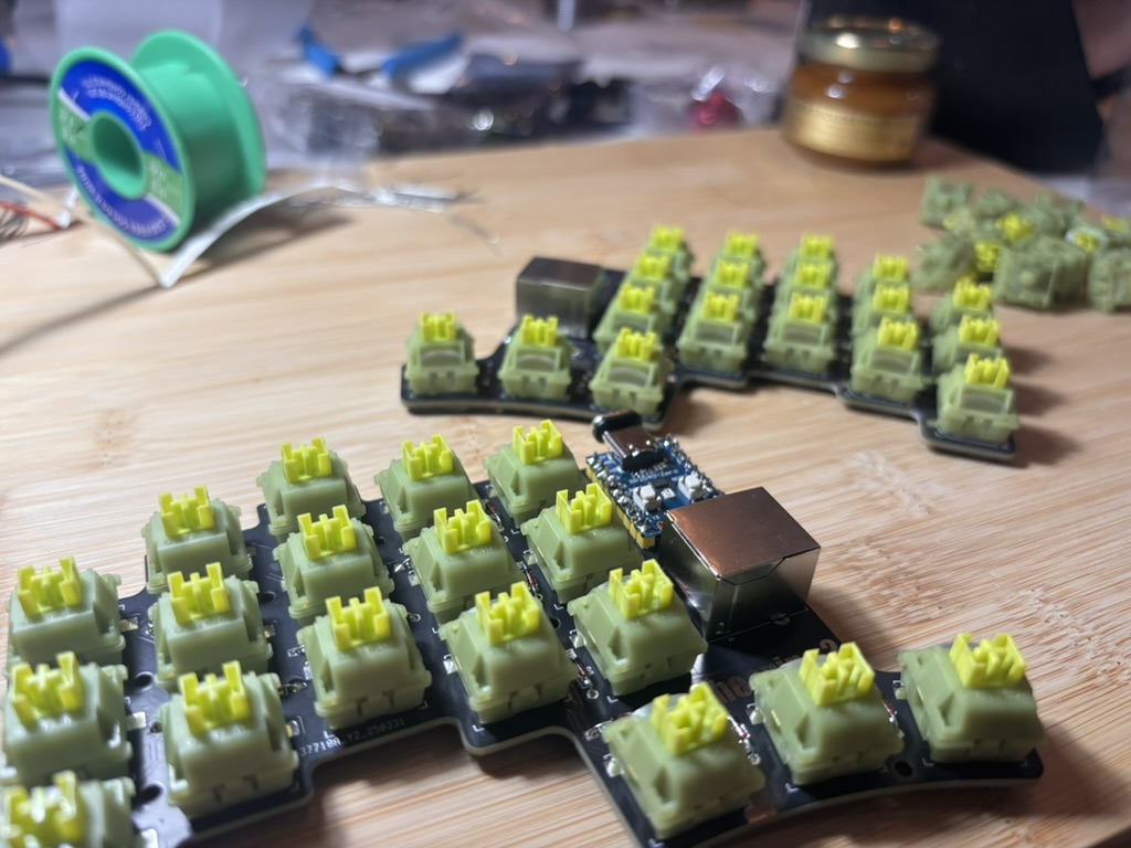 2 PCBs sitting on top of a wooden surface with green switches attached to it